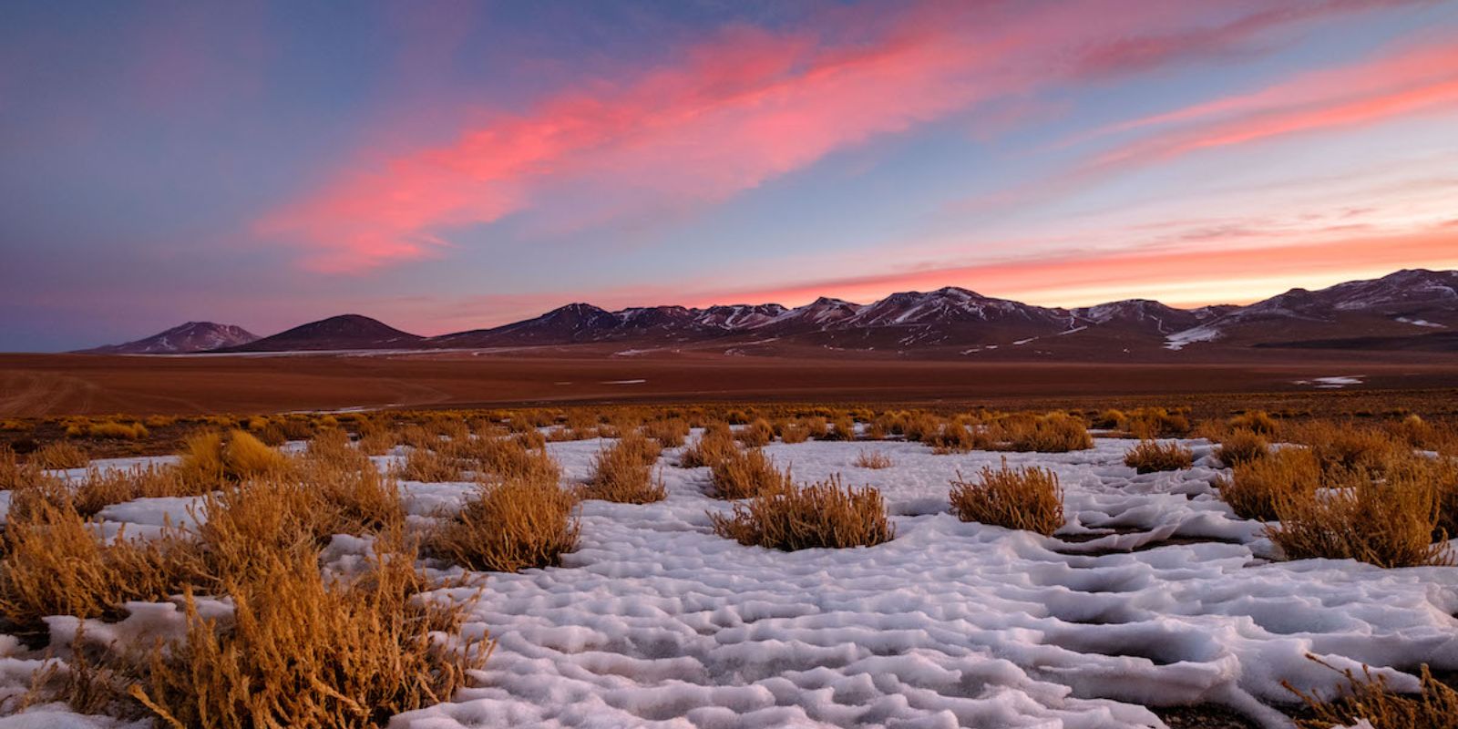 a sunset over a snowy landscape with mountains in the background