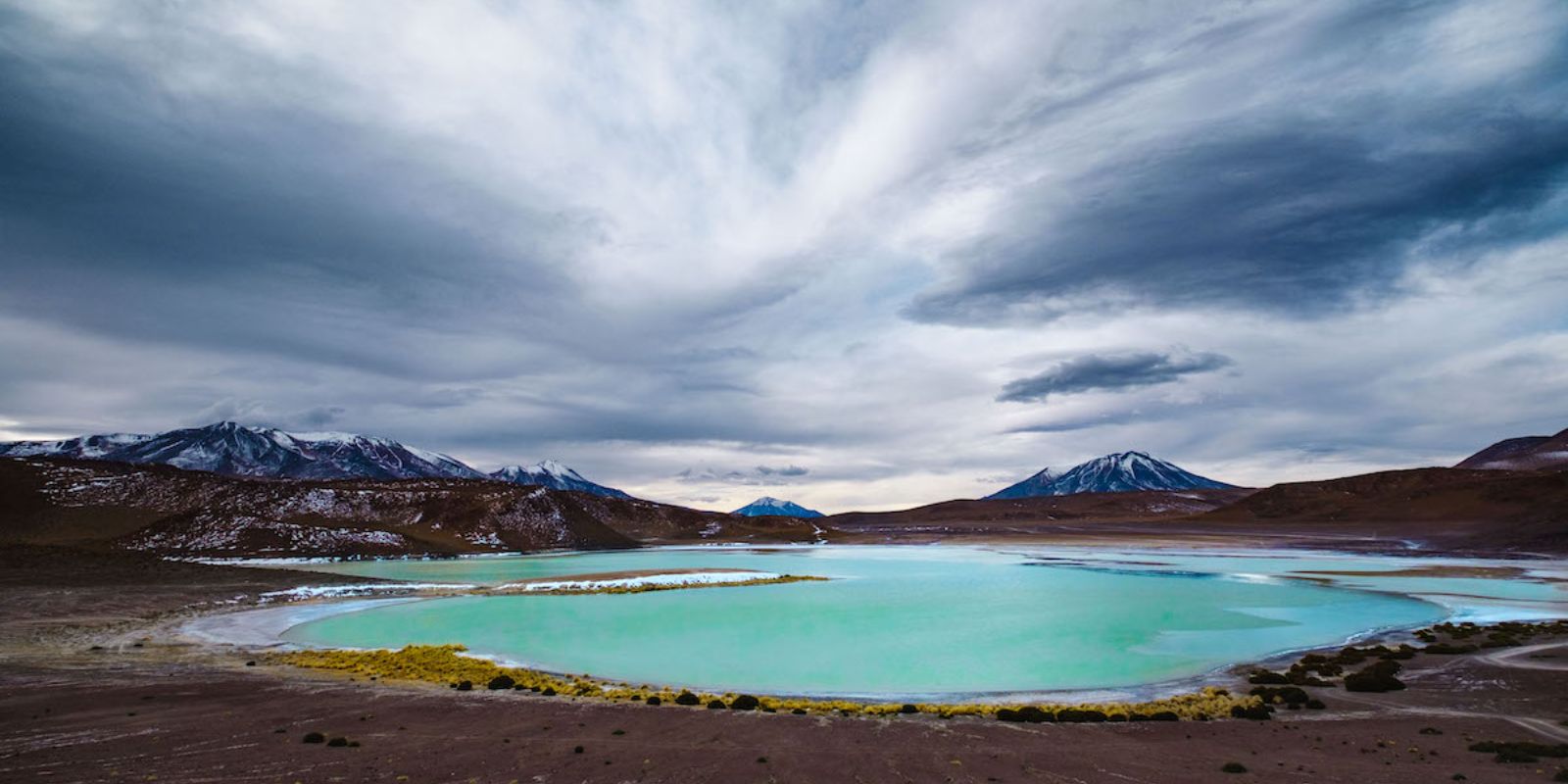 a blue lake in the middle of a cloudy sky