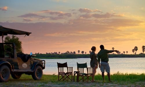 two people standing in front of a safari vehicle at sunset