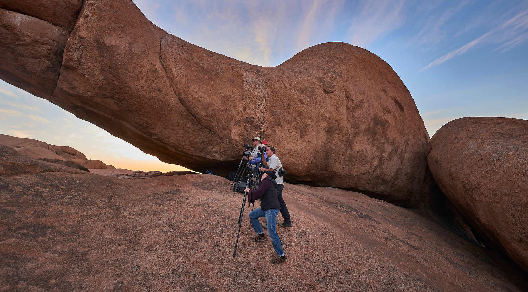 A group of photographers carefully ascends a large rock.