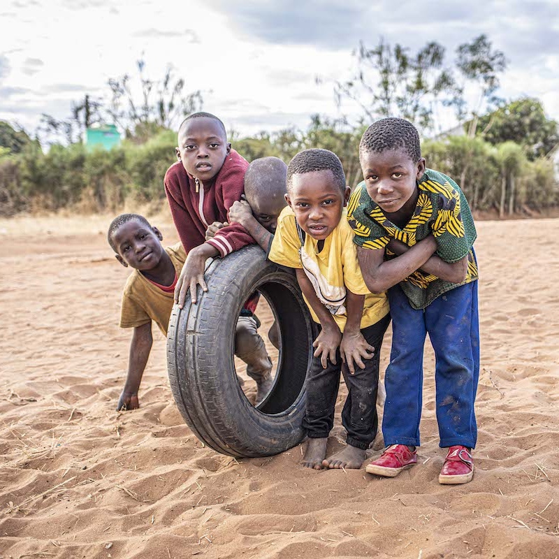 A group of children playing with a tire on sandy ground