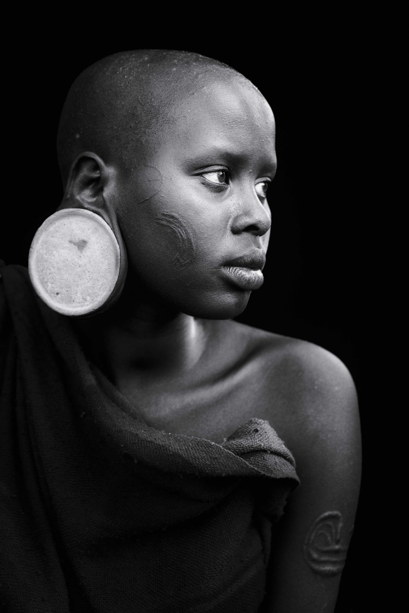 black and white portrait of a woman with tribal markings and a large earlobe disc
