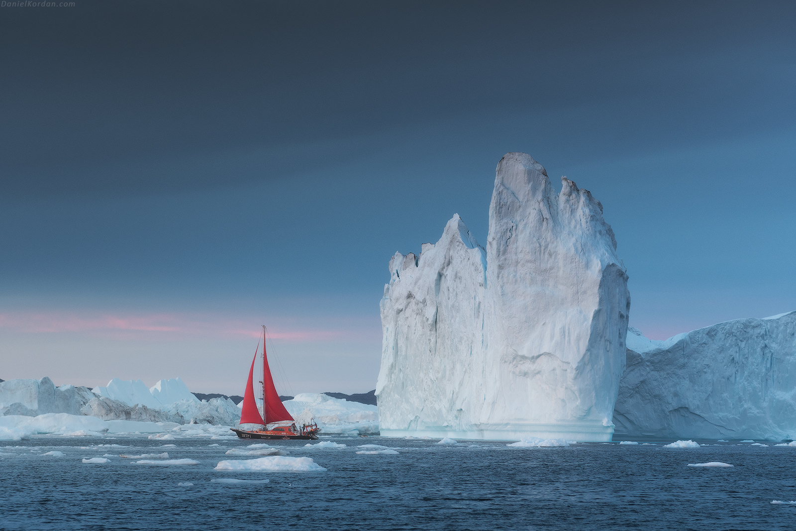 Red sailboat navigating through icy waters beside towering white icebergs