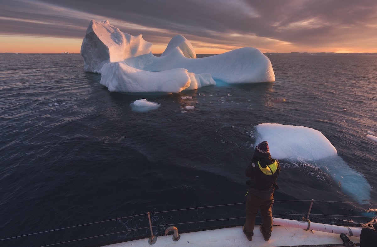 Person on a boat watching a large iceberg at sunset in Arctic waters