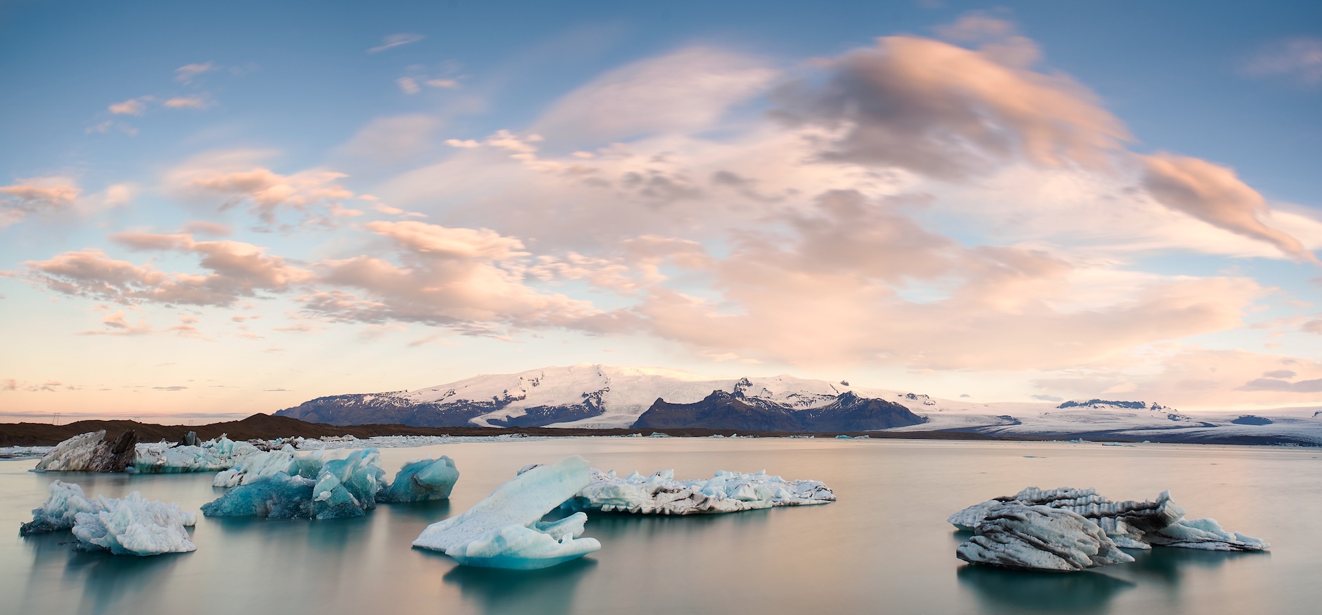 Icebergs floating on a calm lake with snowy mountains