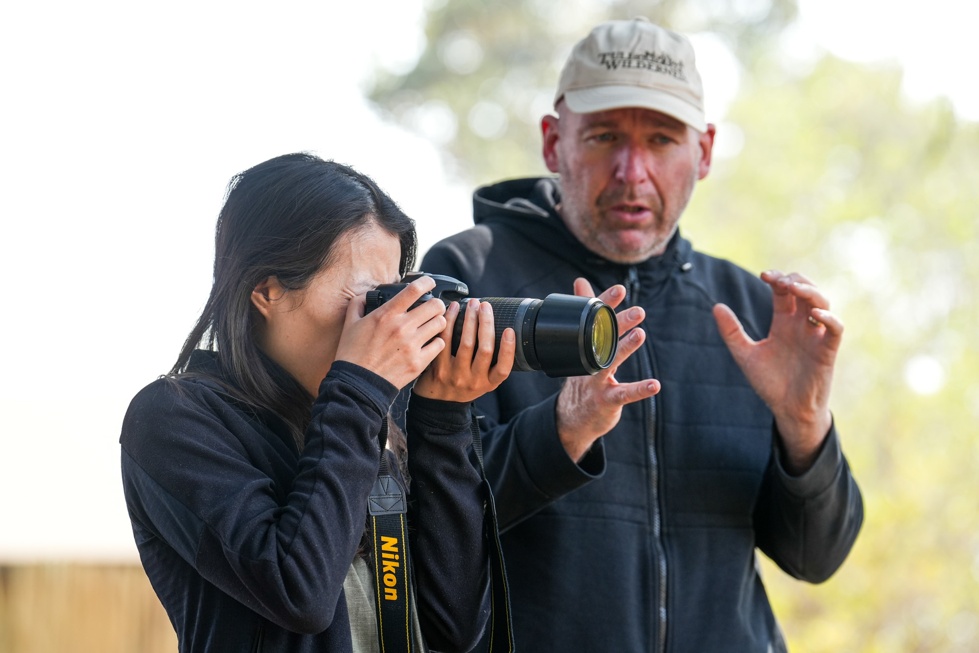 Woman taking a photo with a camera while a man gives instructions