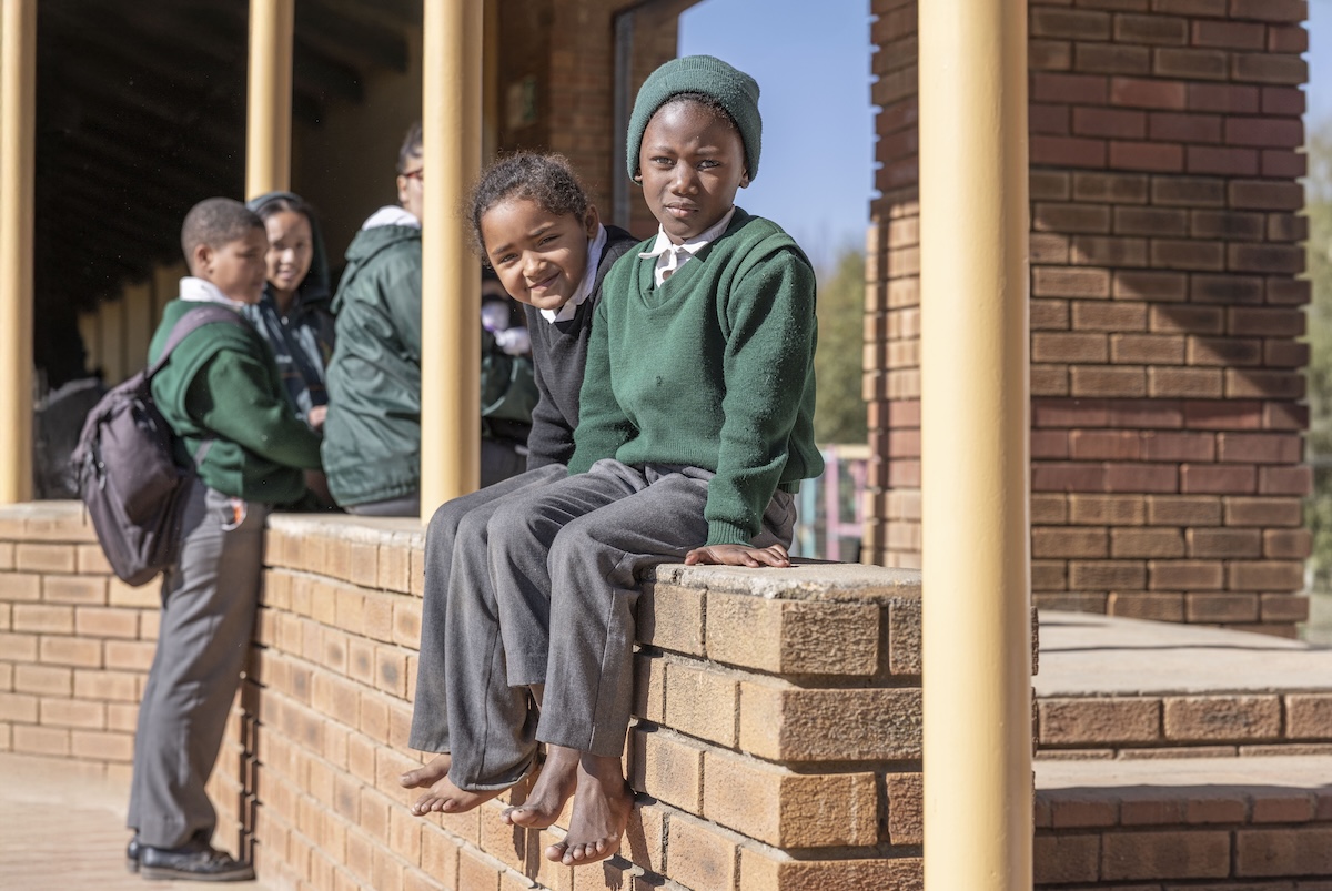 Two barefoot schoolchildren sitting on a wall