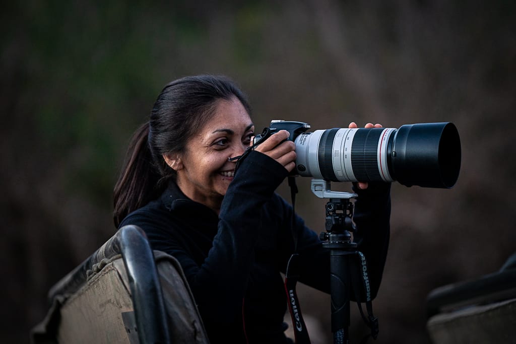 Smiling woman using a camera with a large lens mounted on a tripod