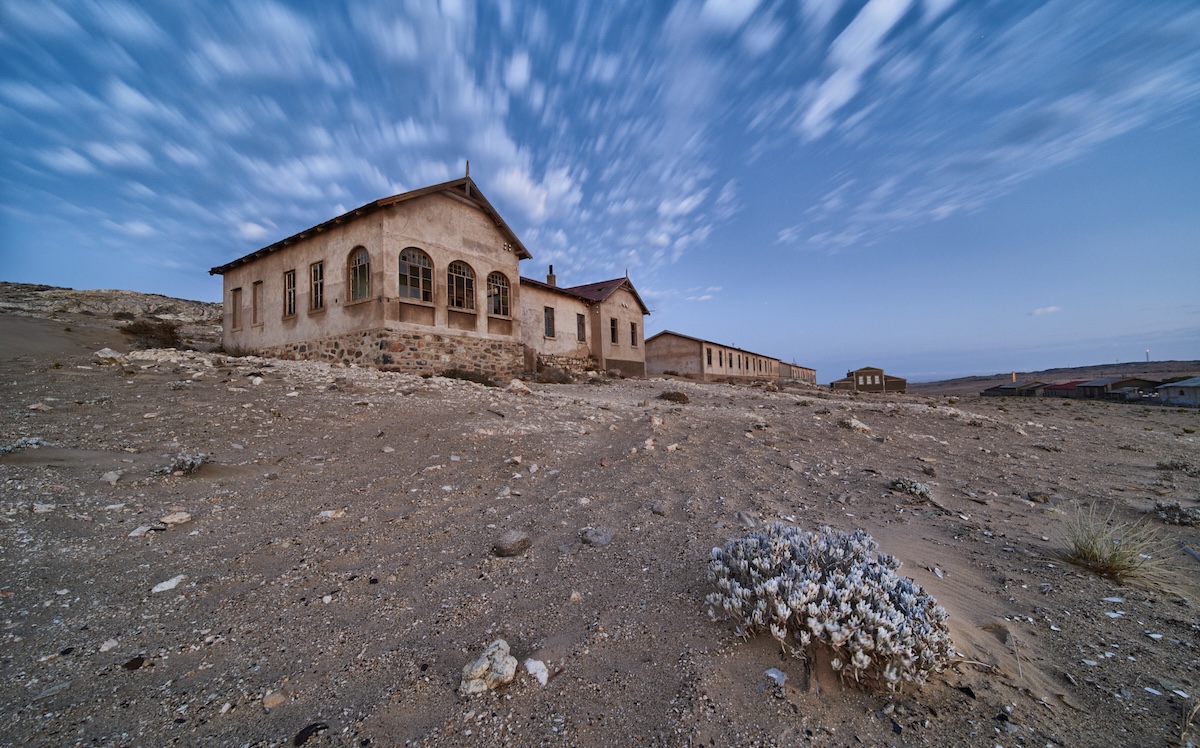 Abandoned buildings in a desert landscape under a cloudy blue sky