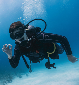 A scuba diver giving the OK hand signal while swimming above a sandy seabed with rising bubbles, captured during an Underwater Photography Workshop on a Penda Photo Tour.