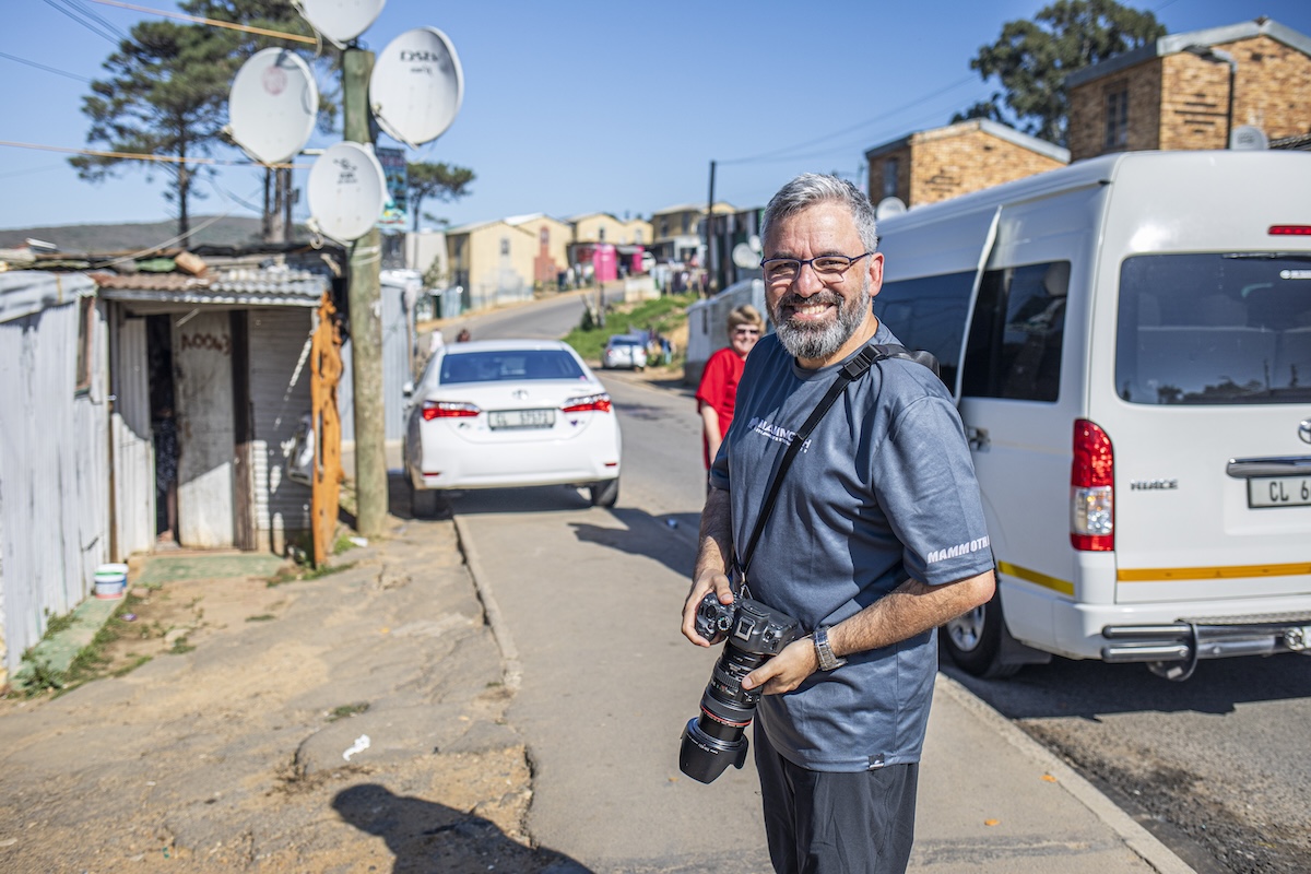 Man smiling with a camera on a sunny street